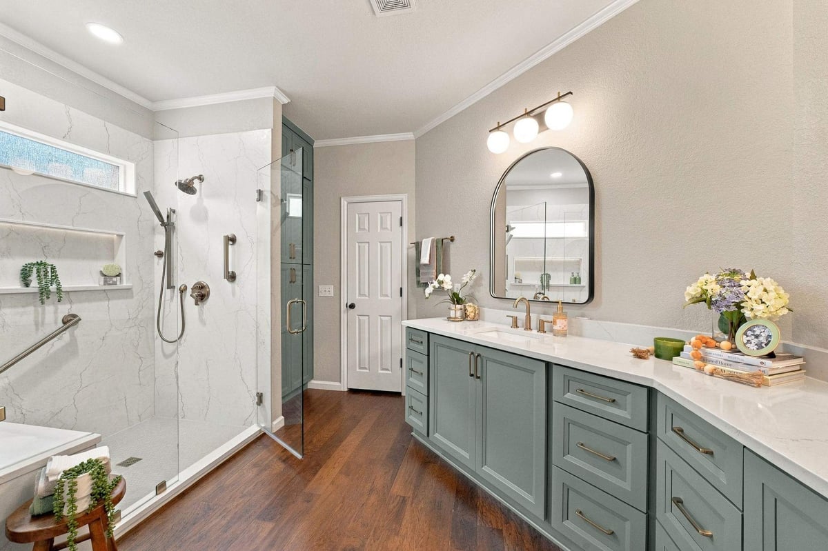 Spacious walk-in shower with frameless glass enclosure, marble-look walls, brass fixtures, and sage-green cabinetry in a San Antonio bathroom remodel.