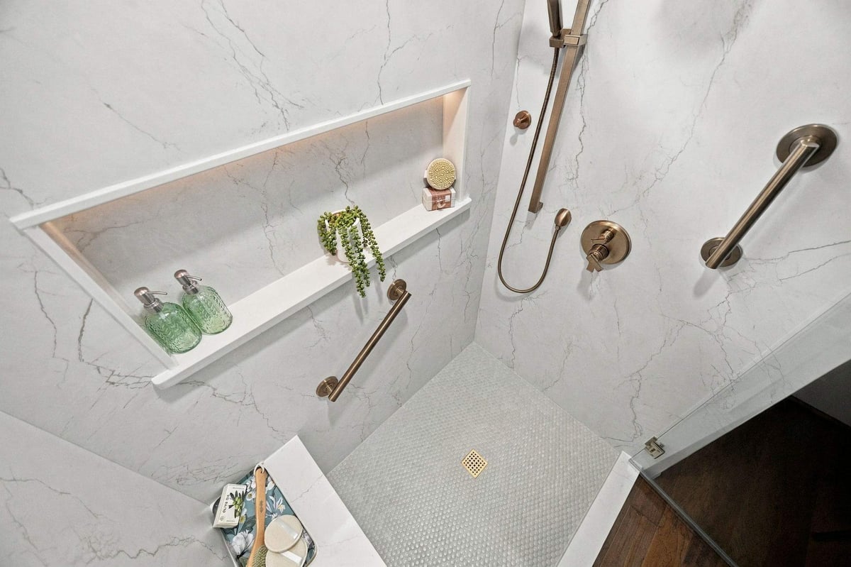 Custom walk-in shower in San Antonio featuring marble-look wall panels, brushed brass shower fixtures, and a frameless glass enclosure.