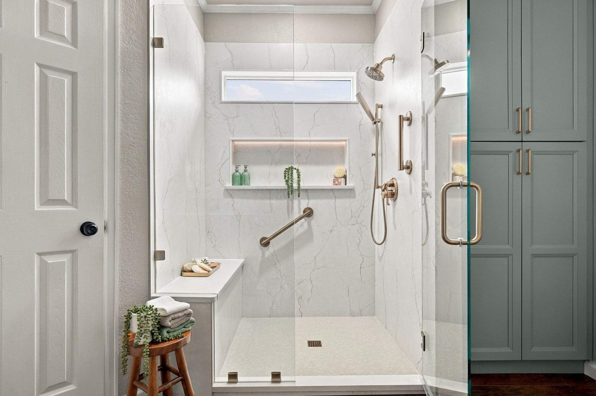 Custom walk-in shower in San Antonio featuring an illuminated shower niche, built-in bench, marble-look walls, and brass fixtures.