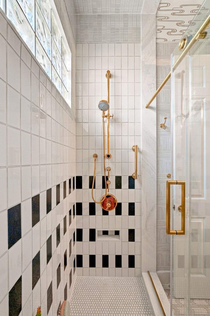 Walk-in shower in a Shavano Park bathroom remodel featuring black-and-white ceramic tile, gold shower fixtures, and glass block windows.