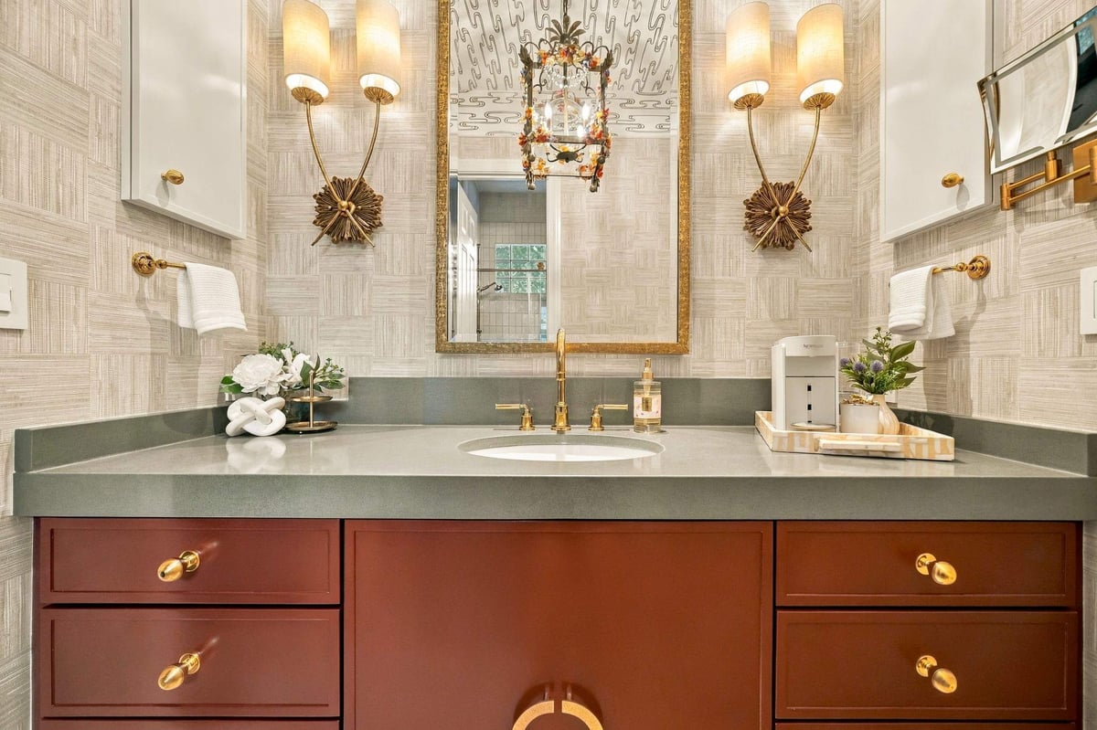 Shavano Park guest bathroom remodel featuring a burgundy vanity, gray countertop, gold fixtures, and decorative wall sconces.