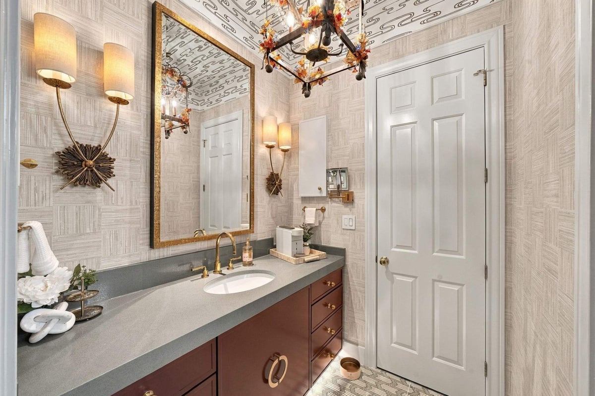 Shavano Park guest bathroom remodel featuring a burgundy vanity, gray countertop, gold-framed mirror, decorative lighting, and textured wall coverings.