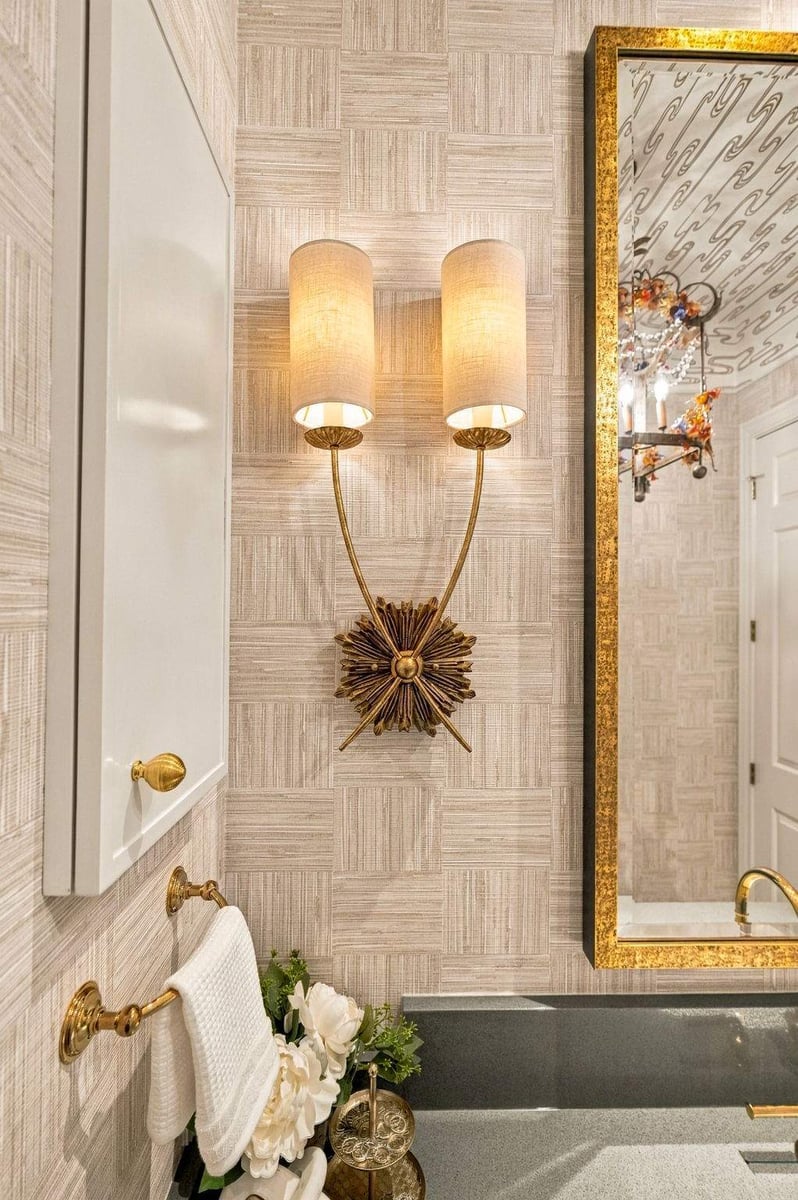 Decorative gold wall sconce, textured wallpaper, and gold-framed mirror in an eclectic Shavano Park guest bathroom remodel.