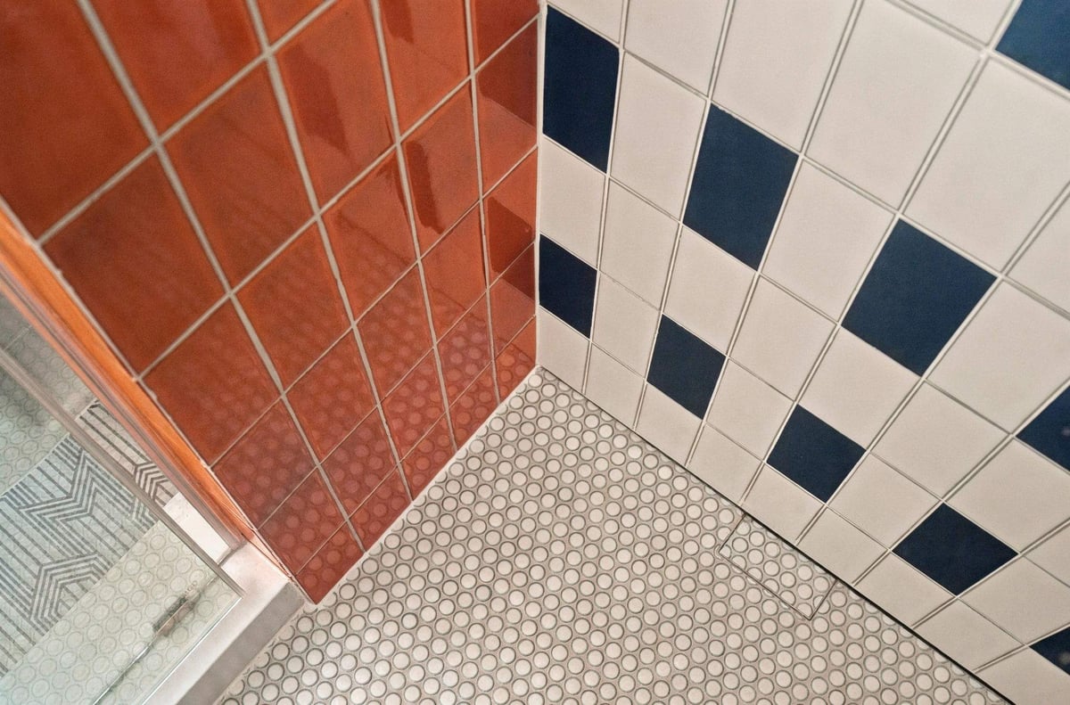 Close-up of vibrant orange ceramic tile alongside black-and-white patterned shower tile with inline drain in an eclectic Shavano Park guest bathroom remodel.