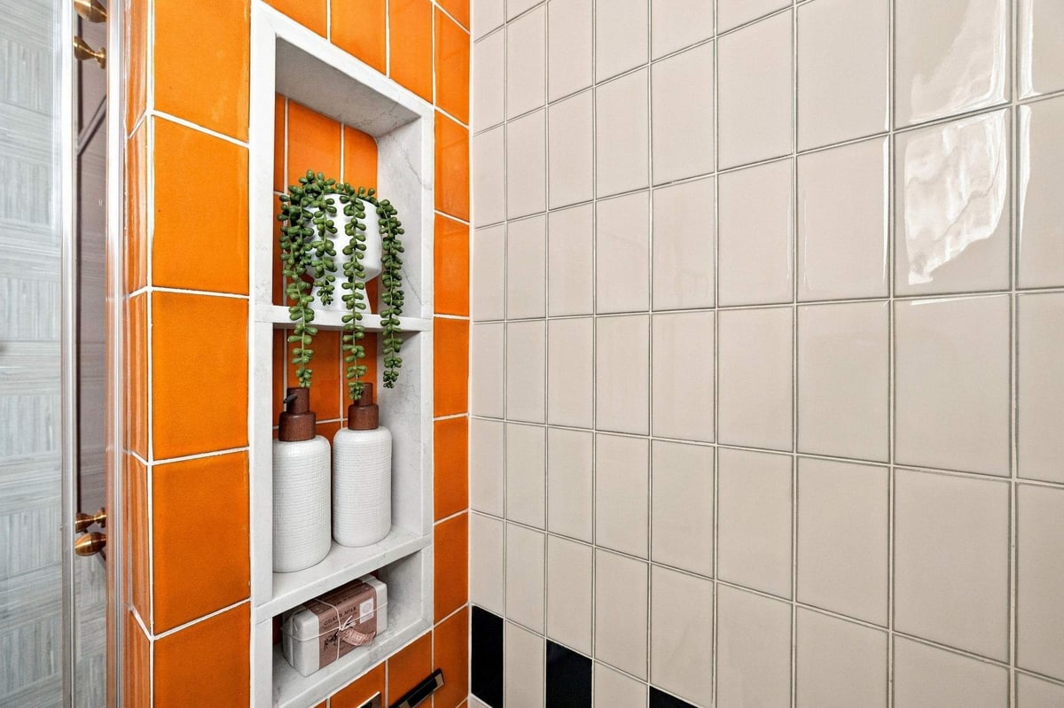 Walk-in shower with vibrant orange ceramic tile, recessed storage niche, and white wall tile in a Shavano Park bathroom remodel.