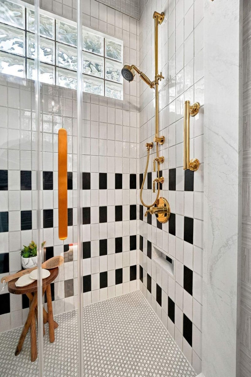 Custom tiled walk-in shower featuring gold fixtures, black-and-white patterned tile, and a glass-block window in a Shavano Park guest bathroom.