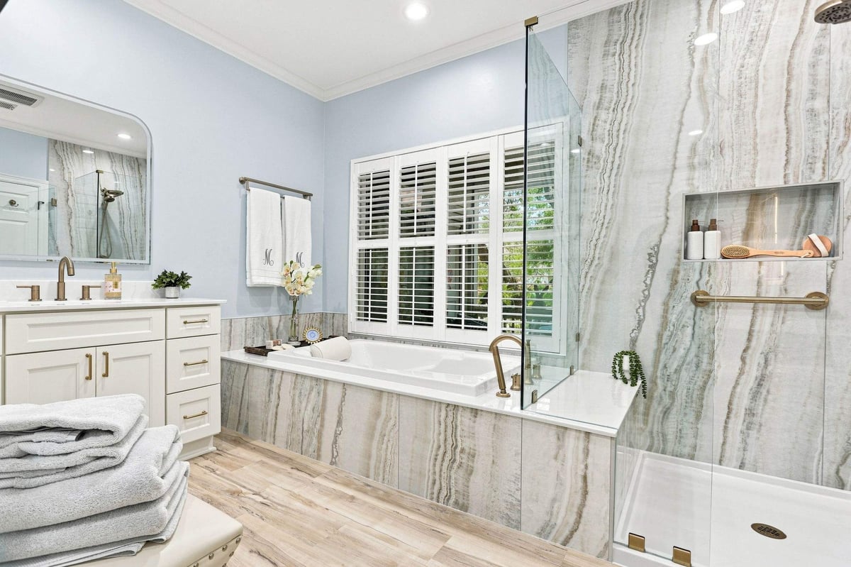 Remodeled primary bathroom with white vanity, jetted bathtub, and glass-enclosed shower.