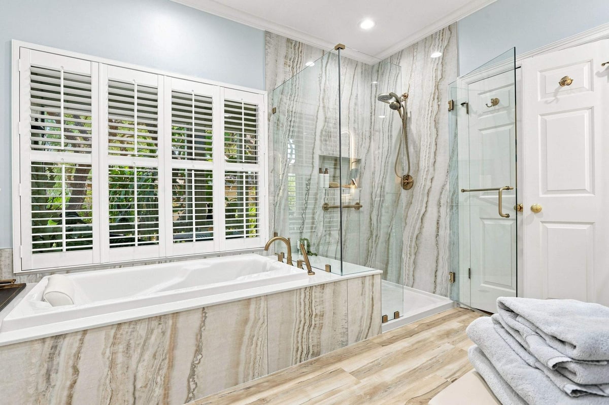 Deerfield primary bathroom featuring a jetted bathtub, walk-in shower, and dramatic natural stone walls.