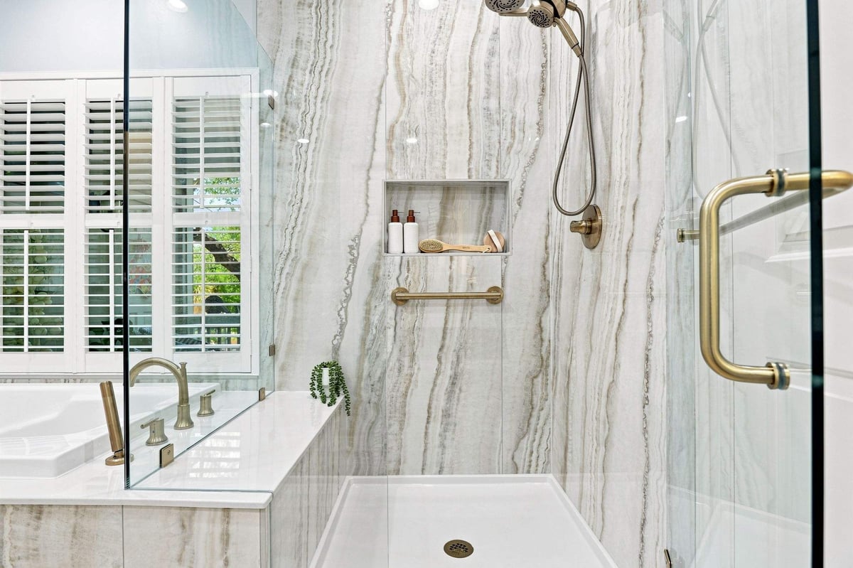 Natural stone shower with recessed niche, brushed-gold fixtures, and glass enclosure.