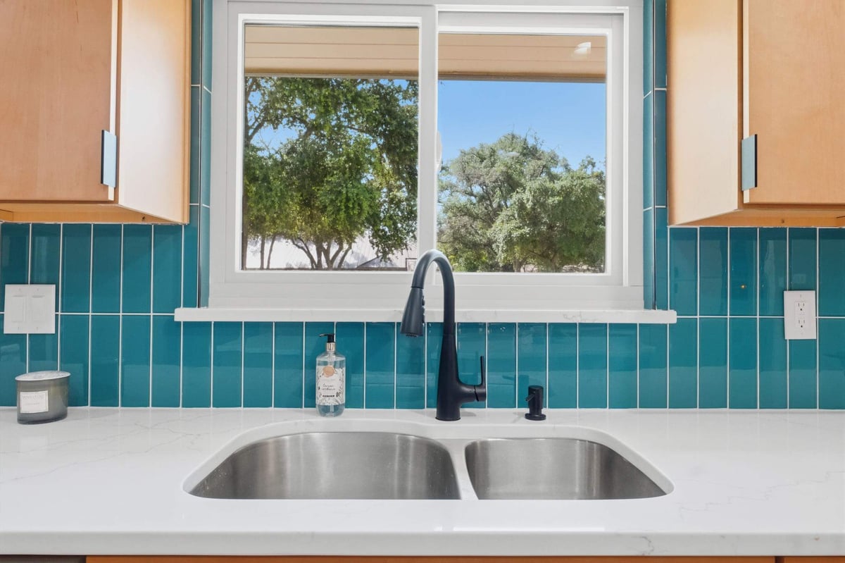 Kitchen sink with black faucet, white quartz countertop and teal tile backsplash