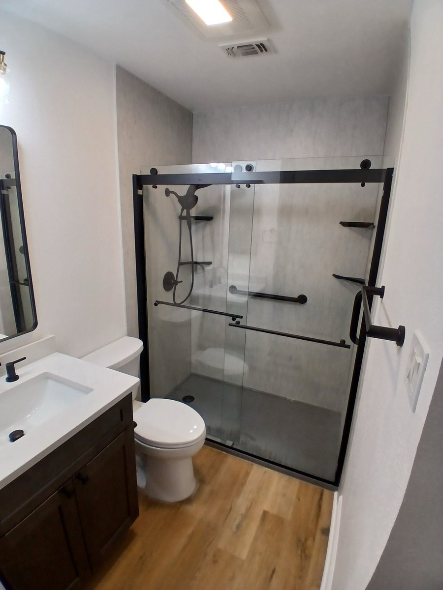 New walk-in shower with glass doors, gray walls, and dark wood vanity