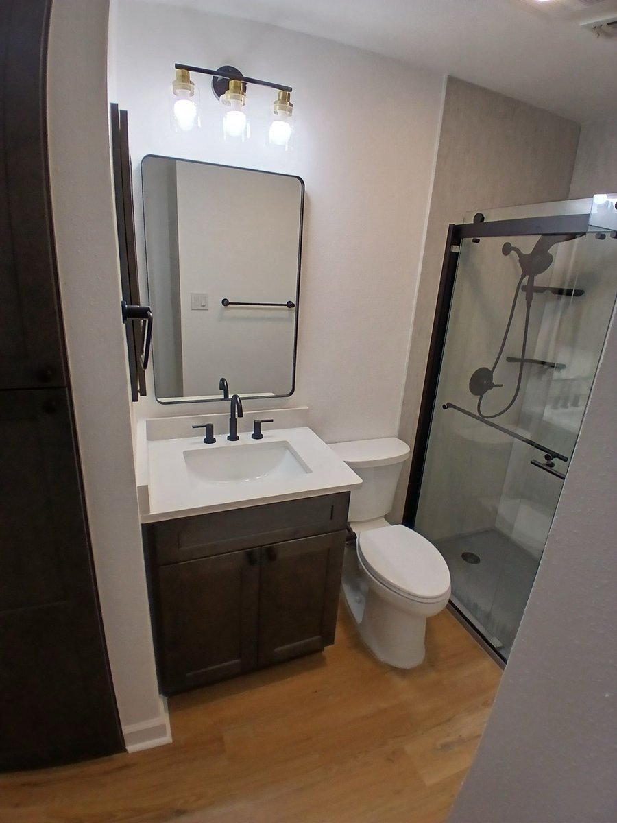 Remodeled bath with dark vanity, framed mirror, and glass-door walk-in shower