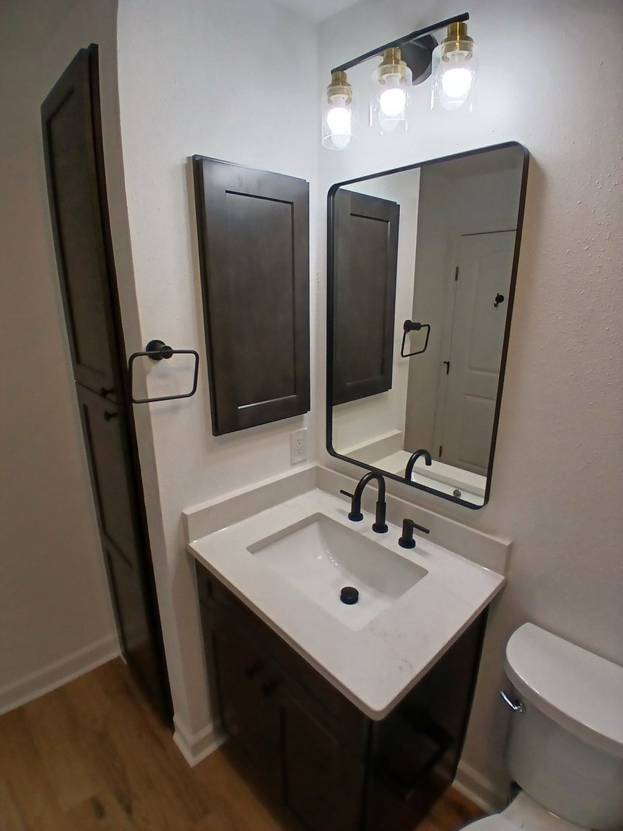 Dark vanity with white quartz top, framed mirror, and linen cabinet