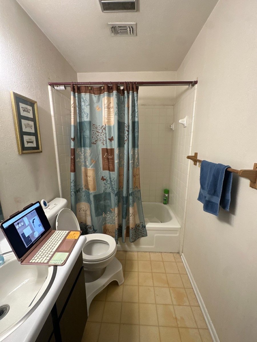 Original dated bathroom with tub-shower, patterned curtain, and beige tile floor
