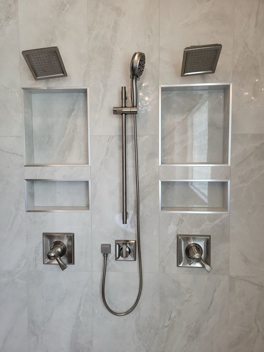 Shower wall with dual rain heads, handheld sprayer, and recessed niches in gray tile