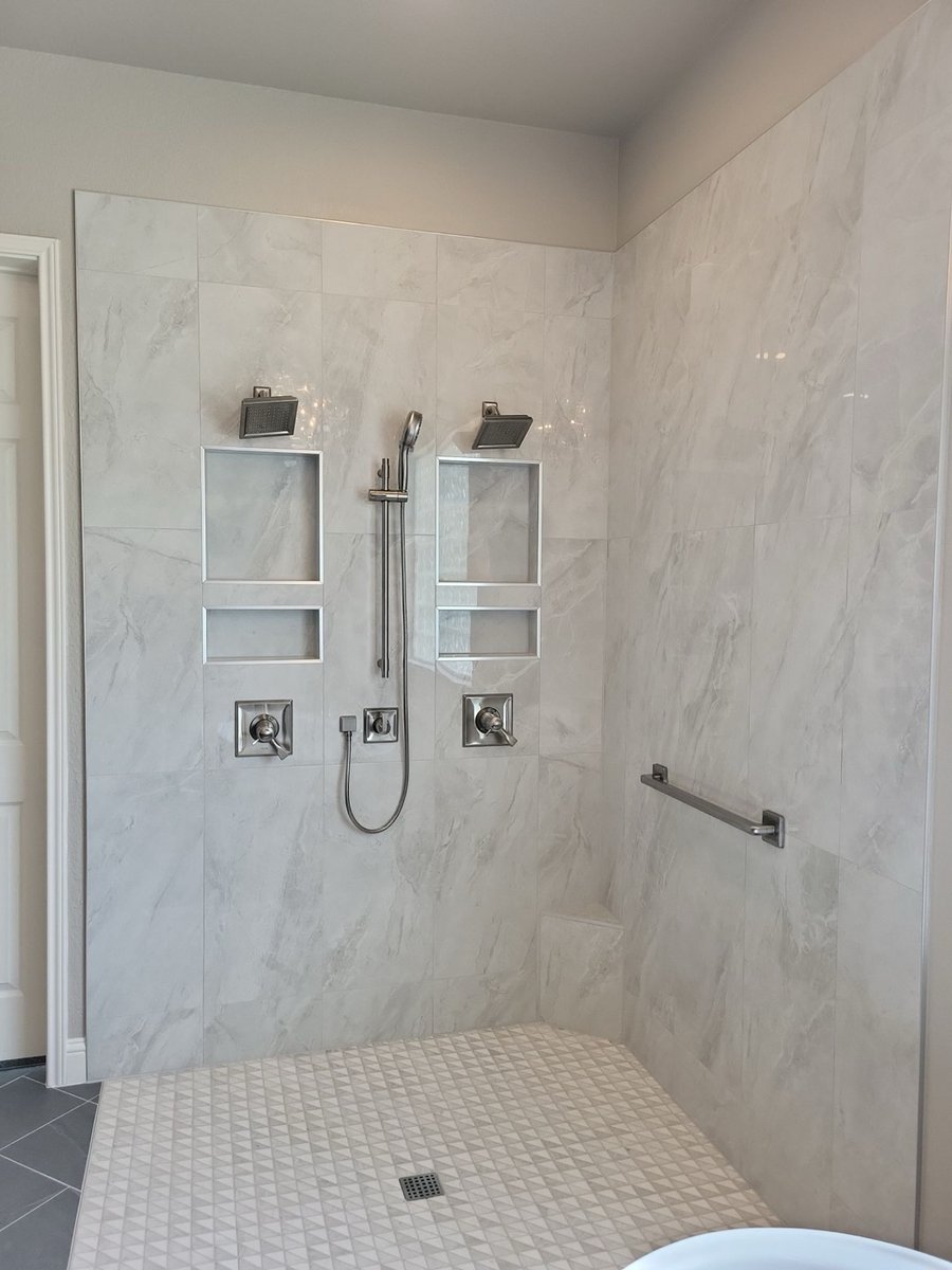 Large gray-tiled walk-in shower with dual heads, niches, and mosaic floor