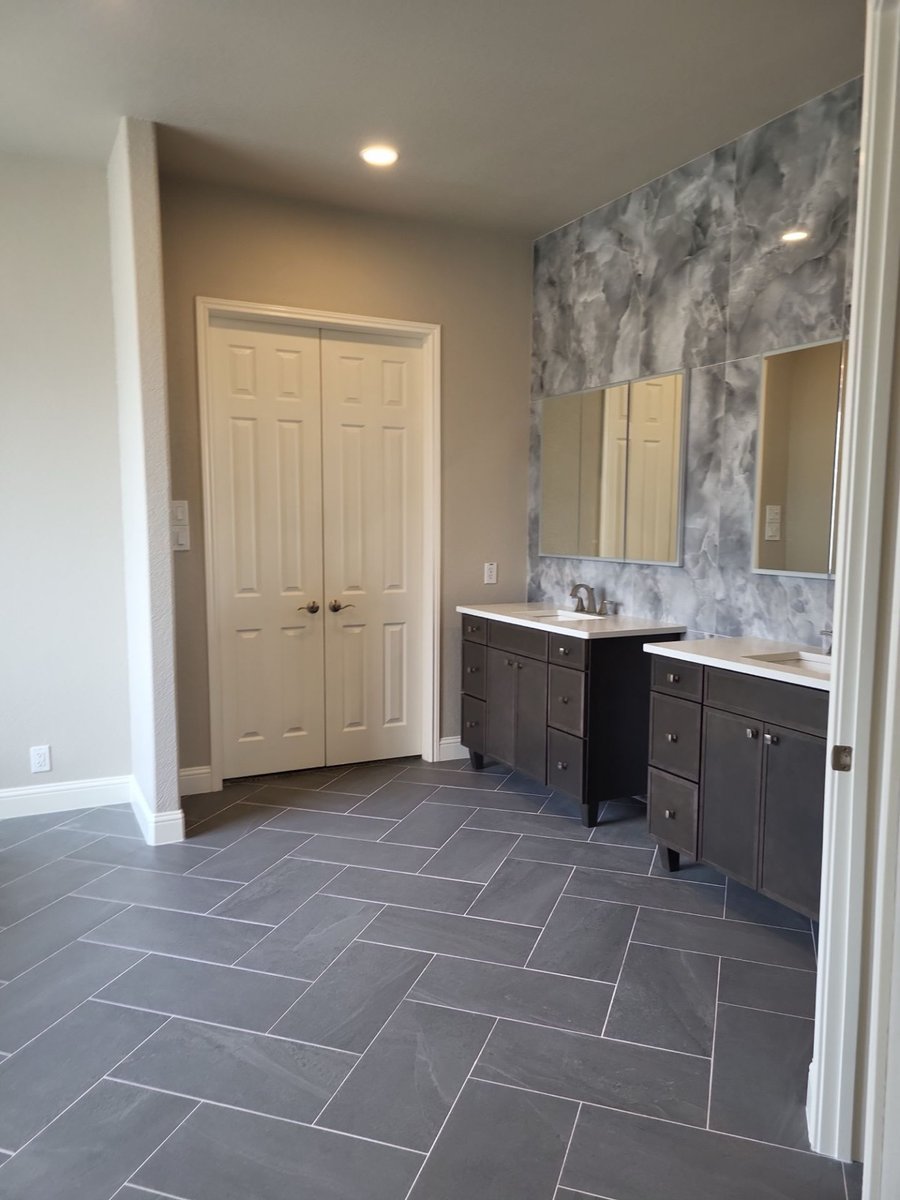 Dual gray vanities with framed mirrors against marble accent wall and herringbone floor