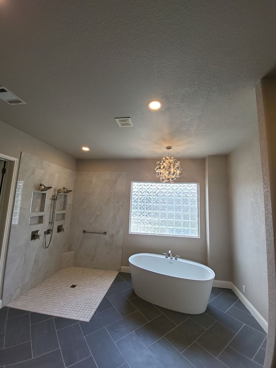 Spacious bath with curbless gray shower, freestanding tub, and glass block window