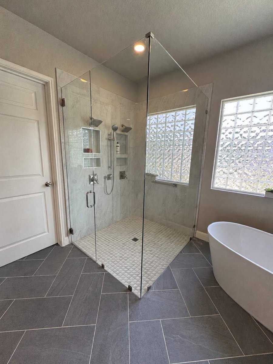 Glass-enclosed corner shower beside freestanding tub and glass block window
