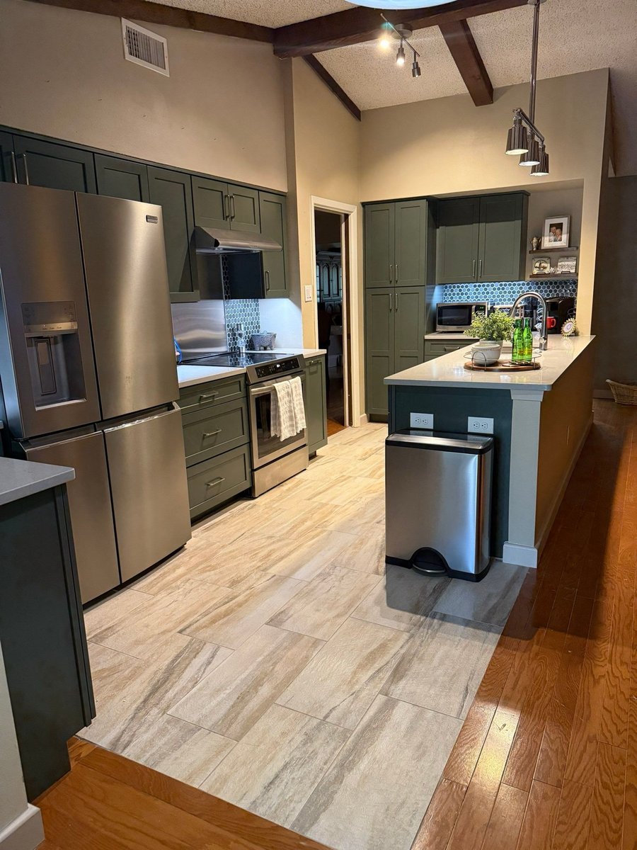 Galley kitchen with green cabinets, stainless appliances and tile-and-wood floor