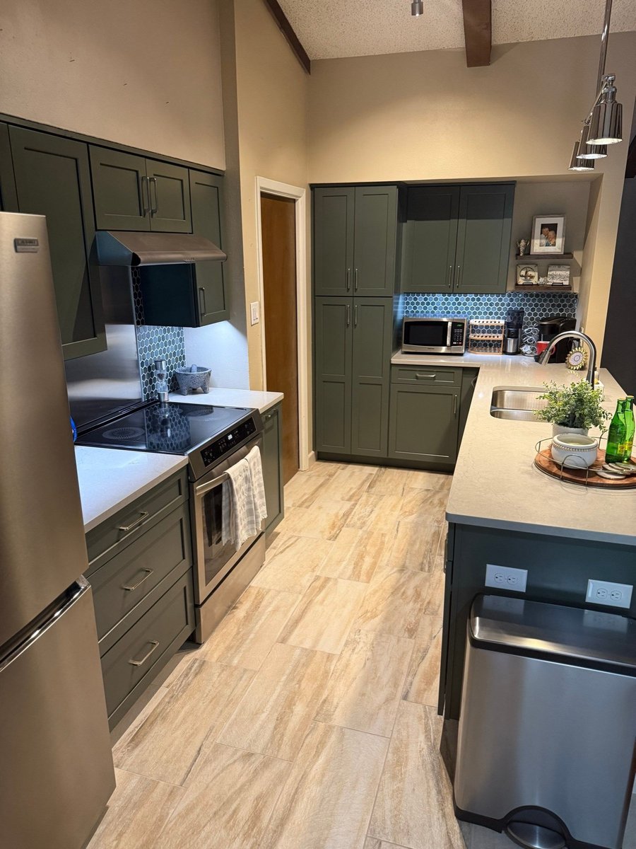 Galley kitchen with green pantry cabinets and tile transitioning to wood floor
