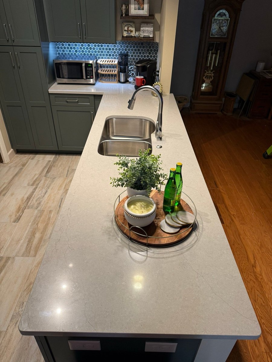 Island counter with undermount sink, decor tray and green cabinets behind