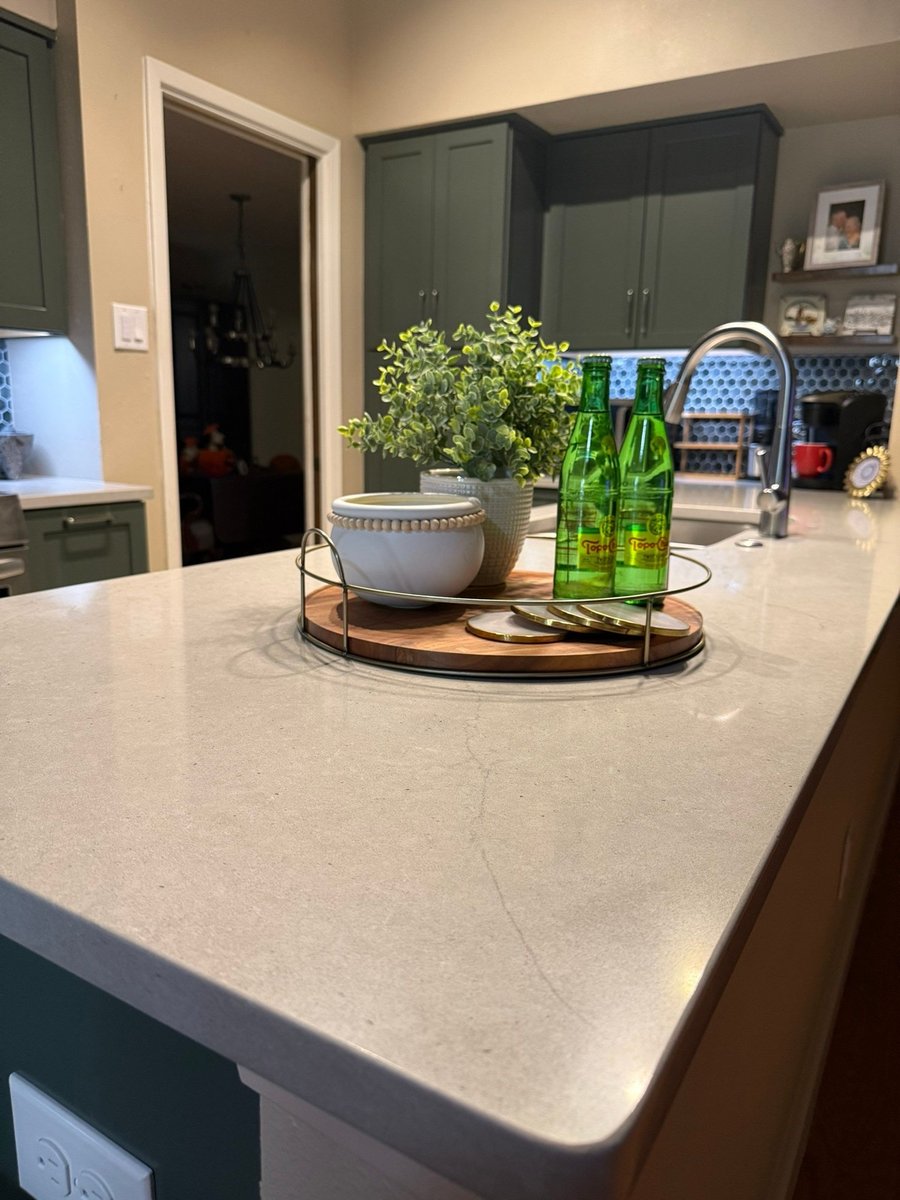 Close view of light quartz island with centerpiece tray and green cabinets