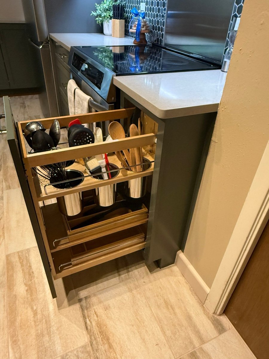 Pull-out base cabinet organizer holding utensils beside green drawers