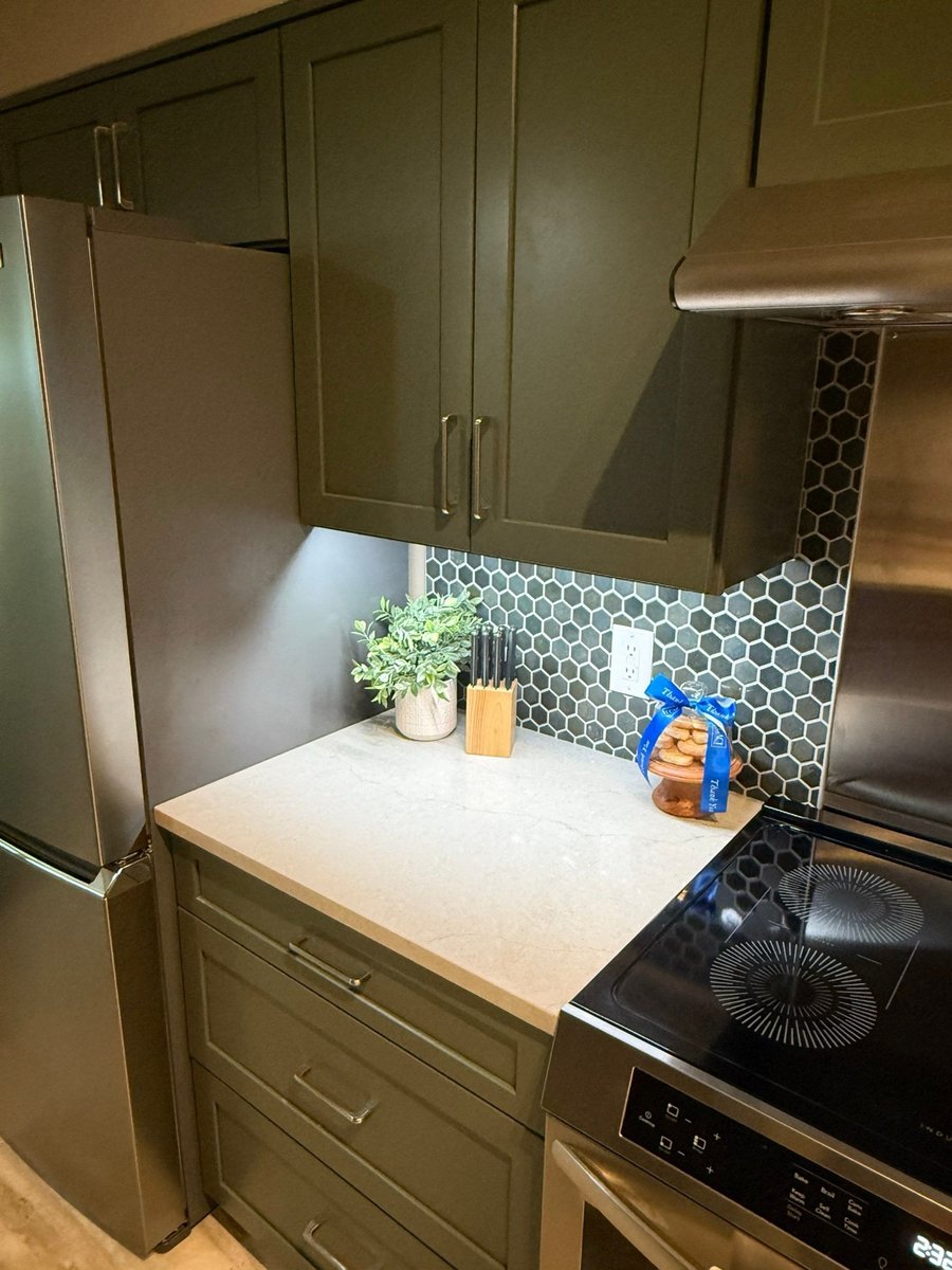 Green cabinets with blue and gray hexagon backsplash beside stainless range