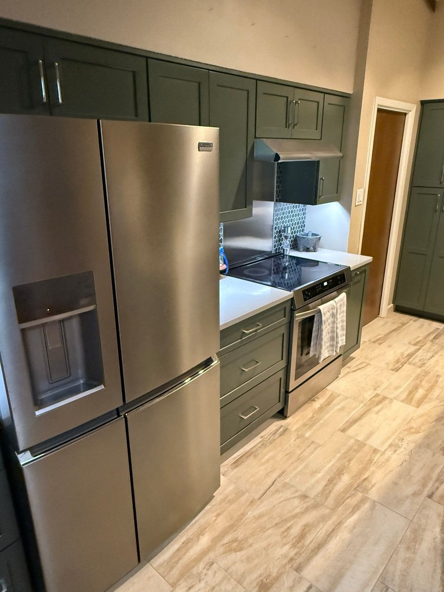 Green base and upper cabinets with stainless fridge and range, tile floor