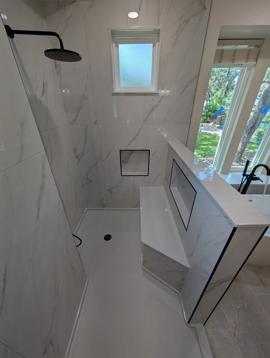 Marble-tiled walk-in shower with black rainfall head and half-wall divider