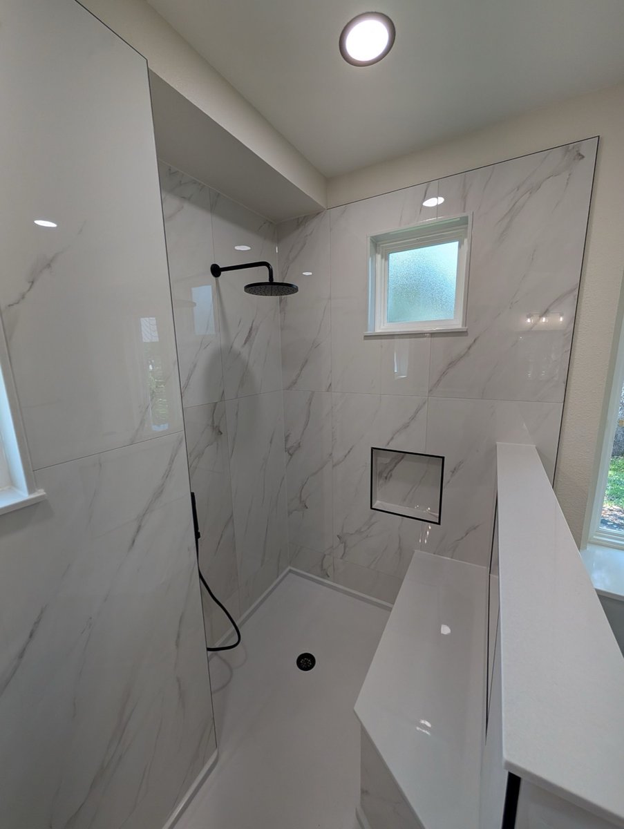 Bright marble-look shower with black fixtures, frosted window and recessed niche
