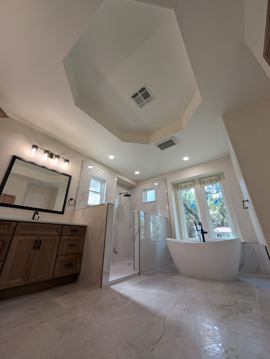 Spacious bath with wood vanity, glass shower and freestanding tub under tray ceiling