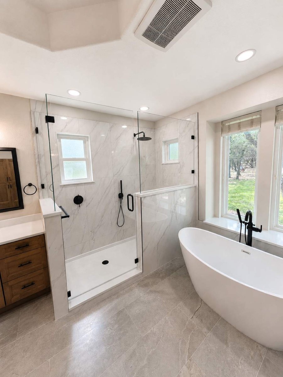 Marble walk-in shower with black hardware next to white freestanding tub