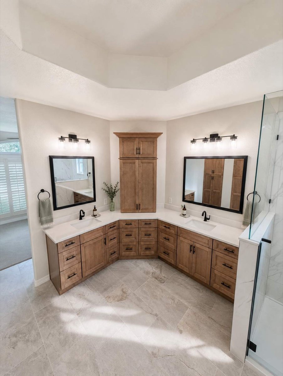 Corner wood vanities with black mirrors flanking tall cabinet under tray ceiling