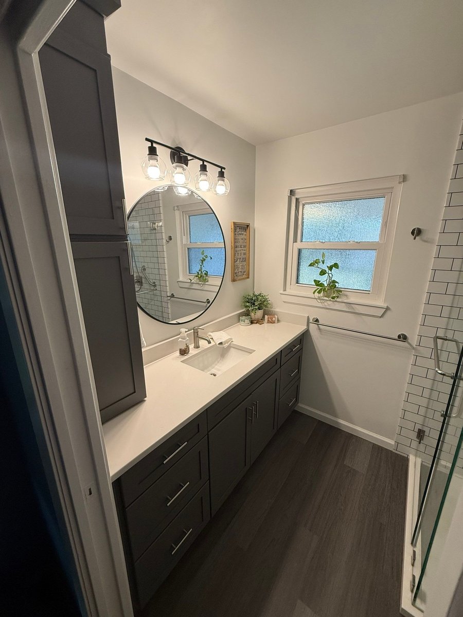 Charcoal vanity with round black mirror and tall linen tower by window