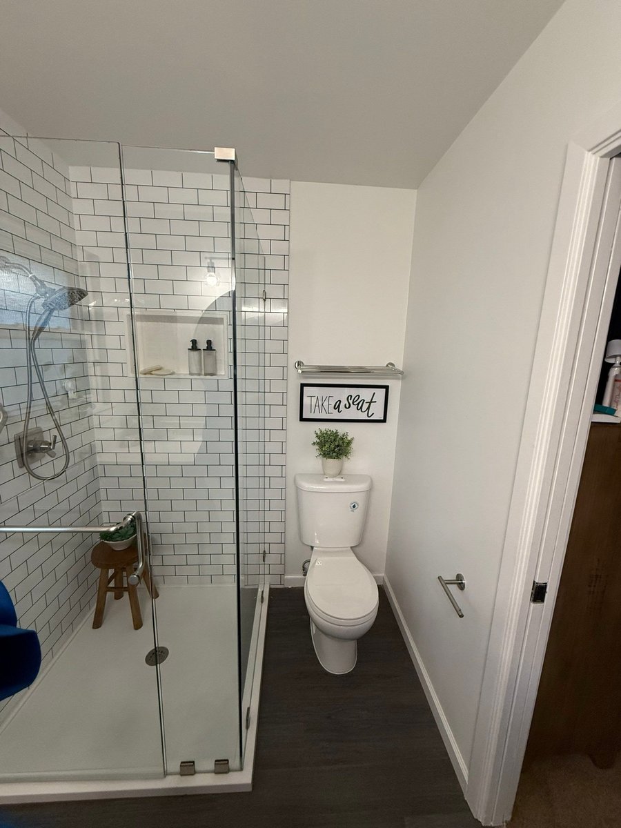 White subway shower with brushed nickel fixtures beside toilet and shelf