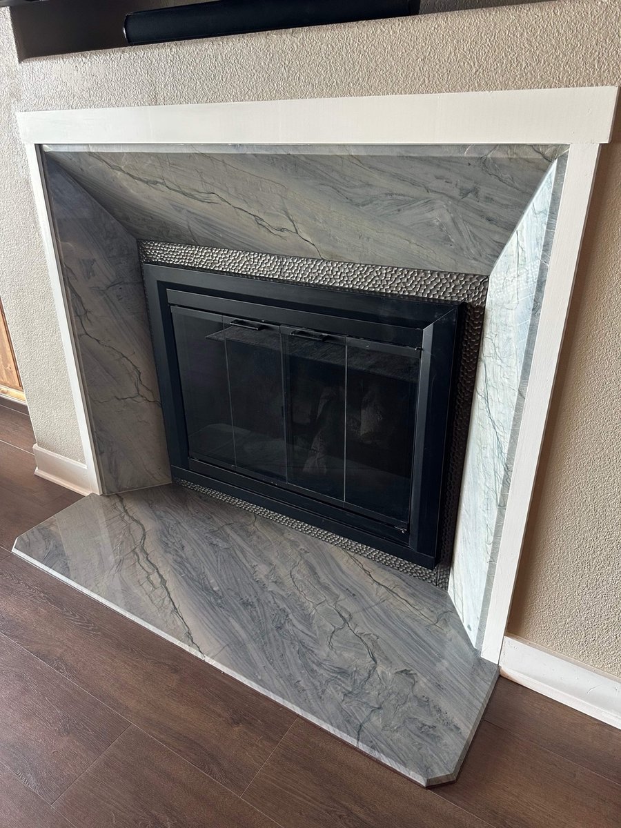 Gray marble fireplace surround with textured tile accent and black glass doors