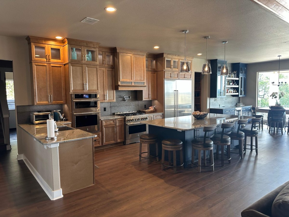 Wide-angle maple kitchen with two islands, range, and bar area with wine bottles