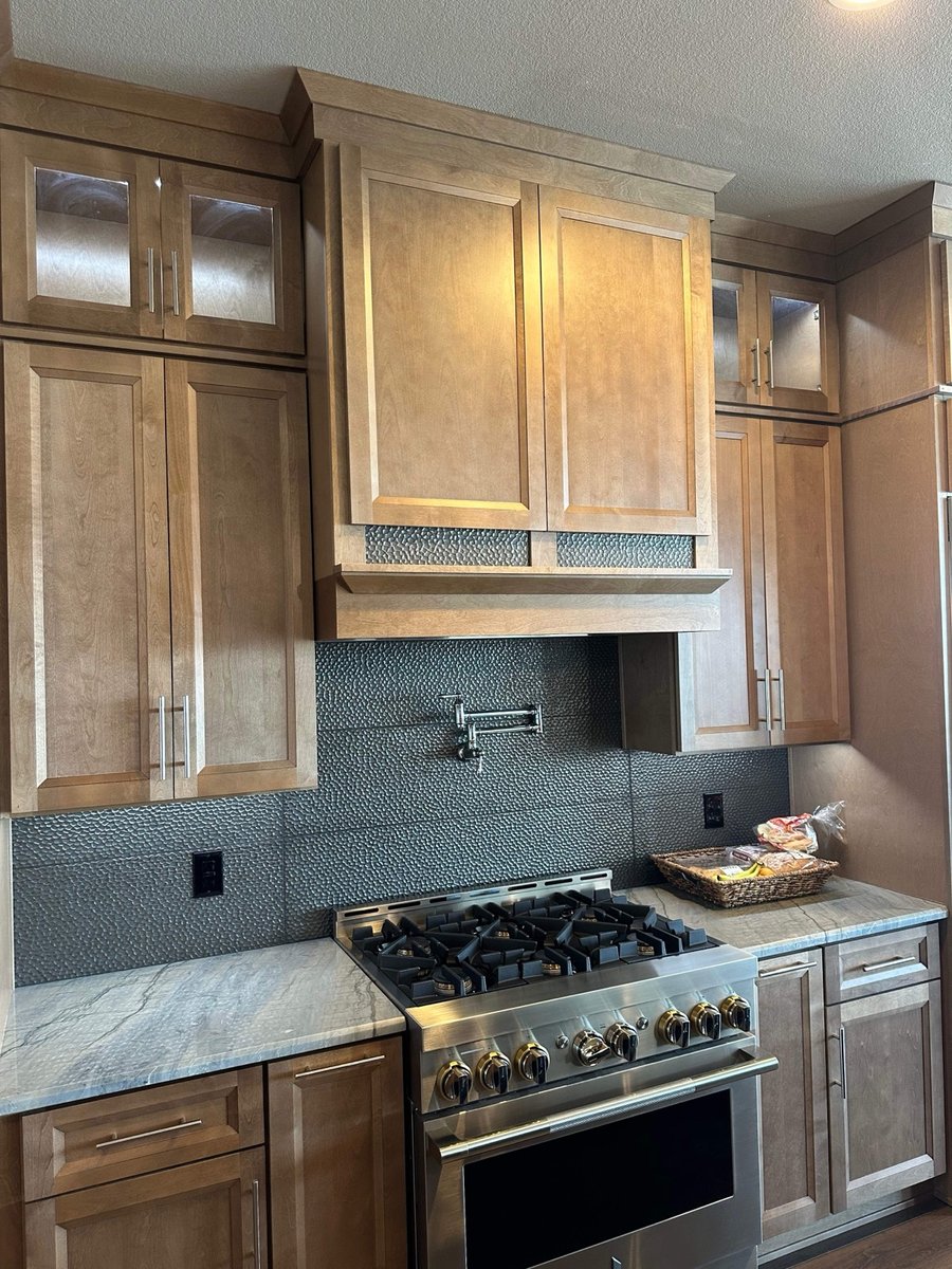 Maple cabinets and stainless gas range below textured charcoal tile backsplash