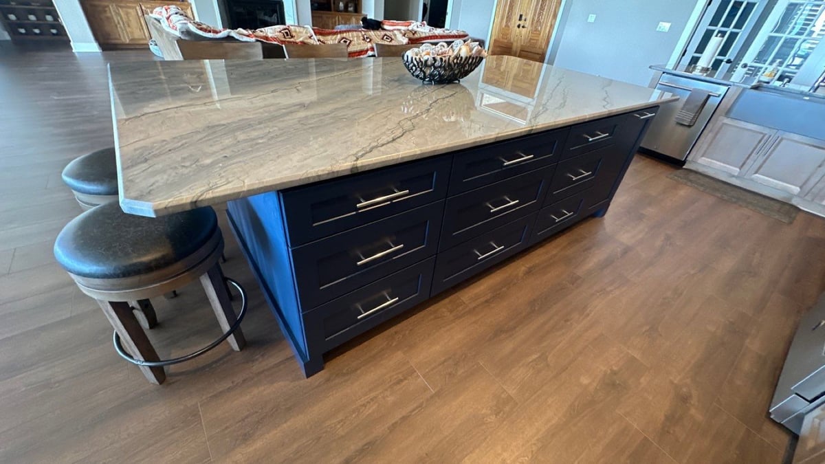 Large kitchen island with veined quartzite top, navy base, and leather counter stools