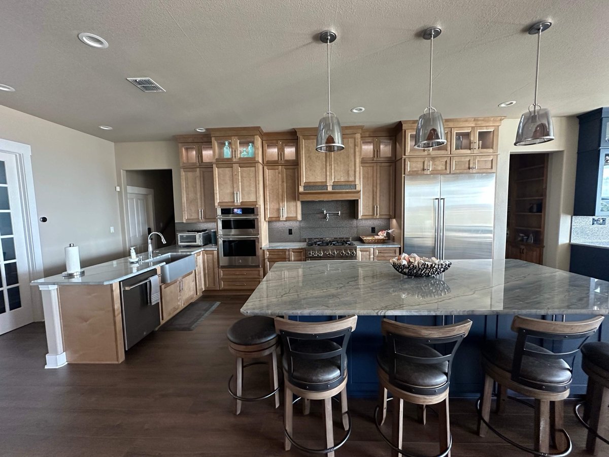 Wide kitchen view with maple cabinets, double ovens, range hood, and seated island