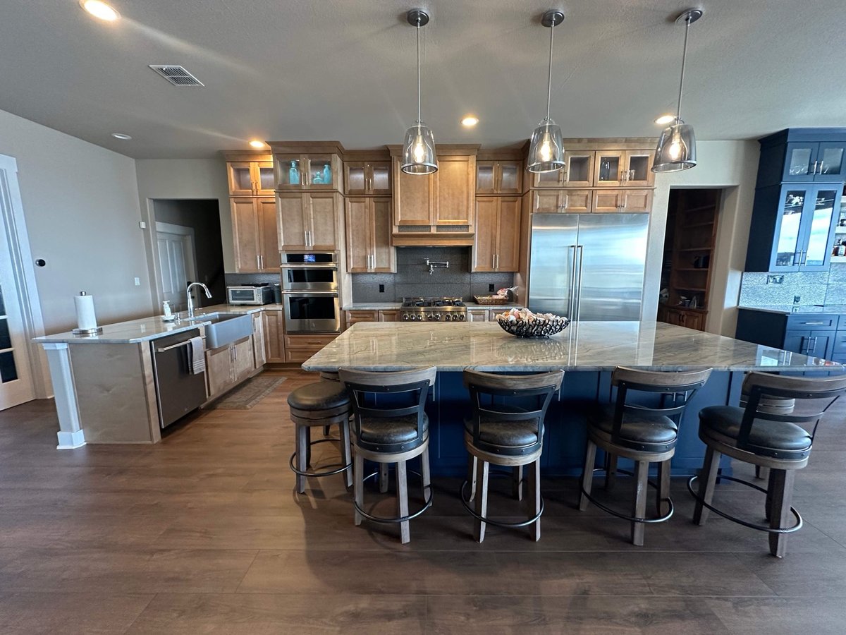 Open-plan maple kitchen with navy island, leather stools, and pendant lighting