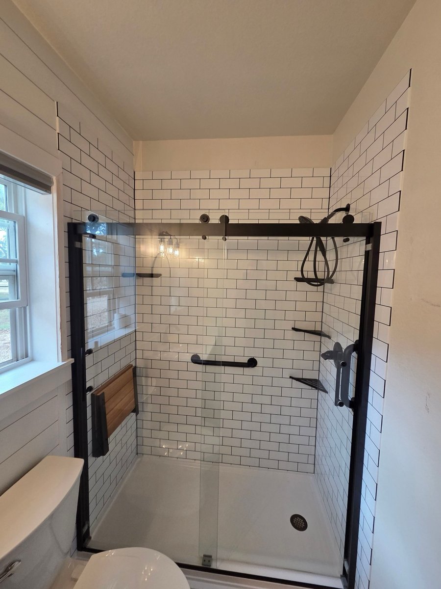Walk-in shower with white subway tile, black fixtures, and sliding glass door