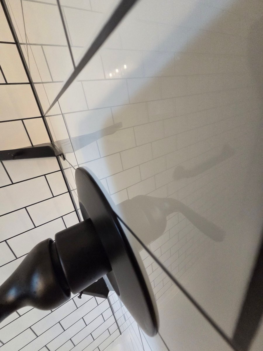 Close-up of black shower control valve against white subway tile