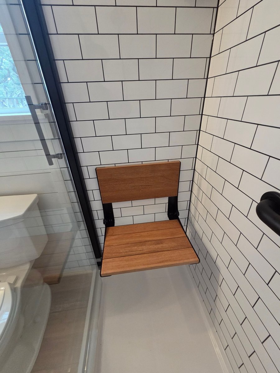 Fold-down wood shower seat against white subway tile with black hardware
