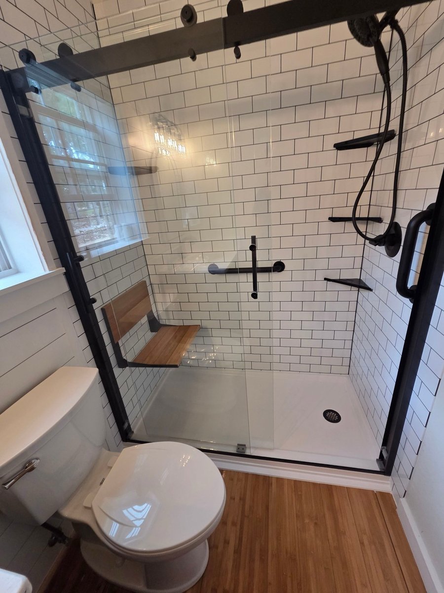 Tub-to-shower conversion with subway tile, wood bench, and black sliding door