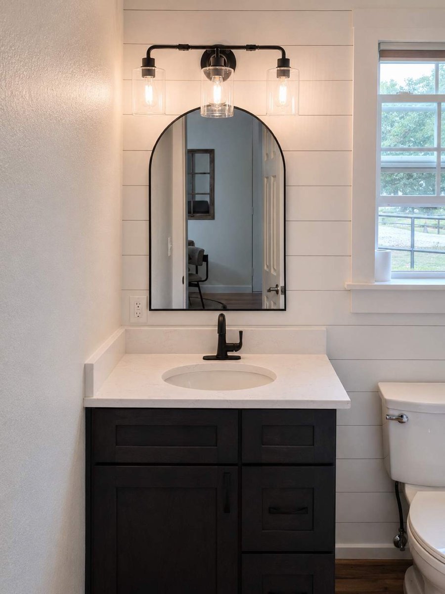 Black vanity with arched mirror, shiplap wall, and three-light fixture