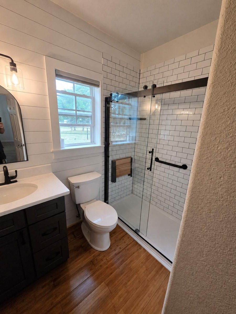Compact bath with black vanity, walk-in subway shower, and wood plank floor