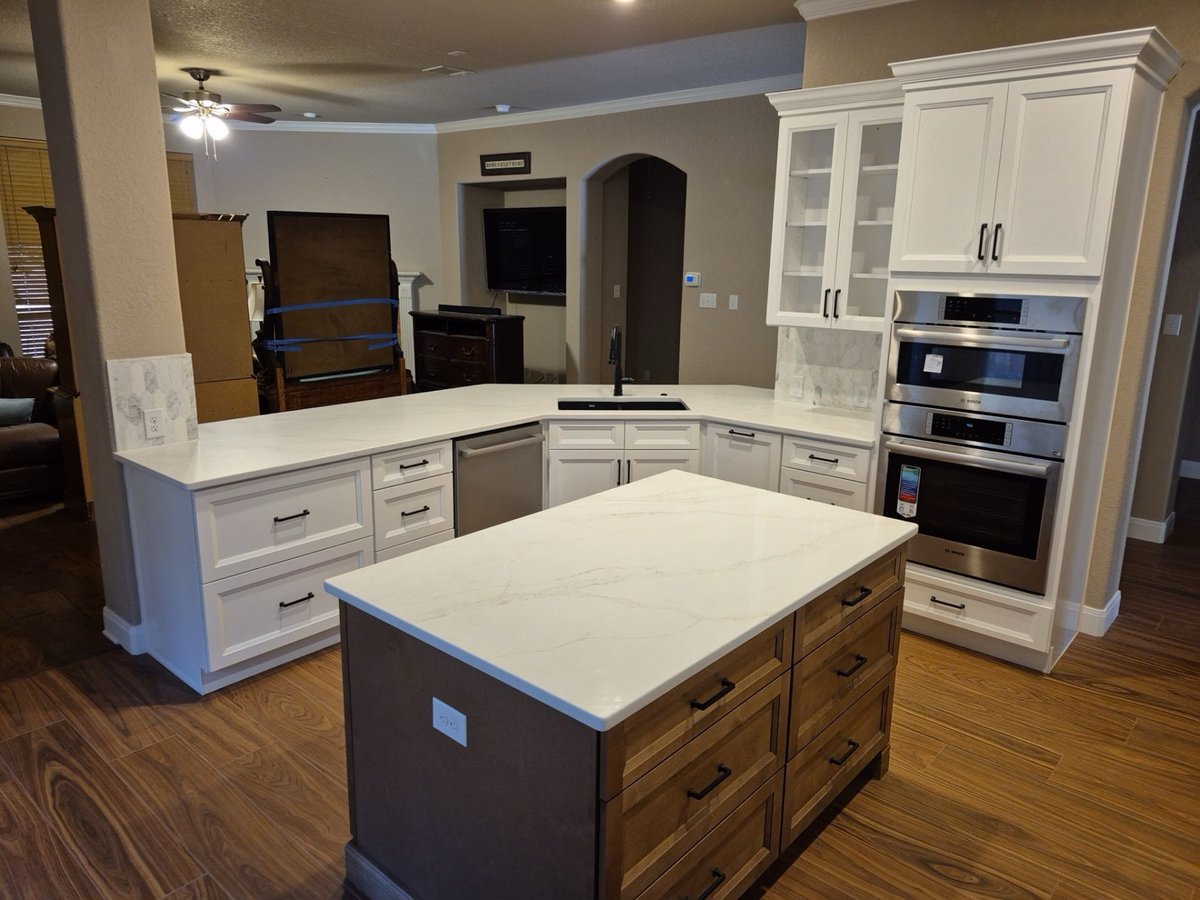 Remodeled kitchen with white cabinets, marble island, and stainless wall ovens